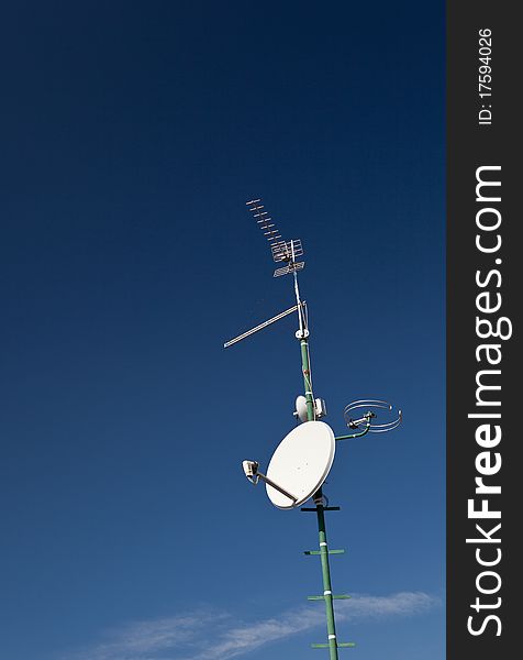 Antennas and a satellite dish on a roof against lovely blue sky