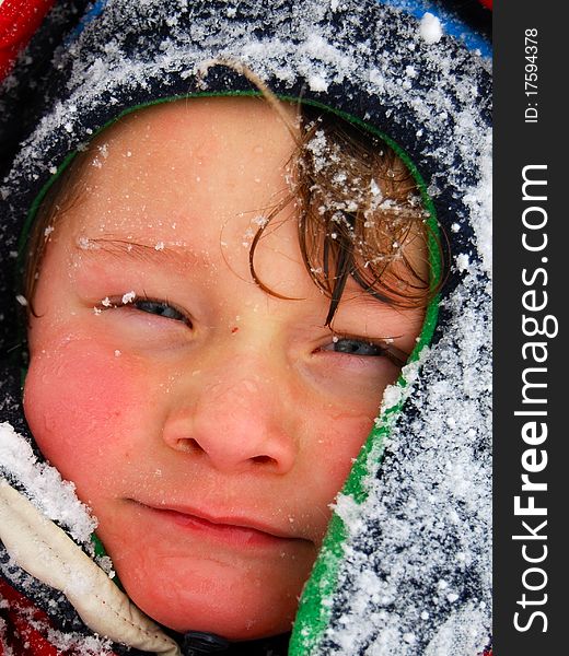 A white caucasian toddler boy of the face wearing a hat and covered with snow. A white caucasian toddler boy of the face wearing a hat and covered with snow.