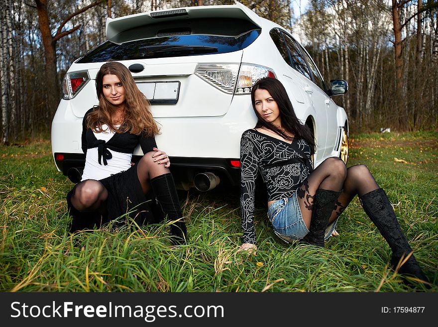 Two beautiful girls friend on the background of the stylish white sports car. Two beautiful girls friend on the background of the stylish white sports car