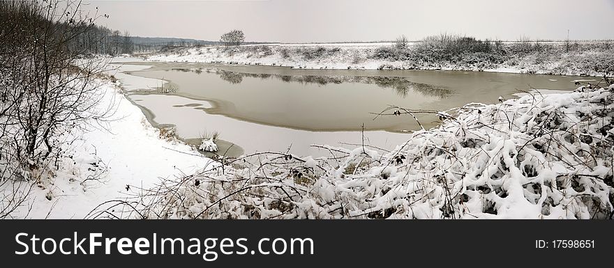 Winter panorama: partially frozen lake near snowy forest