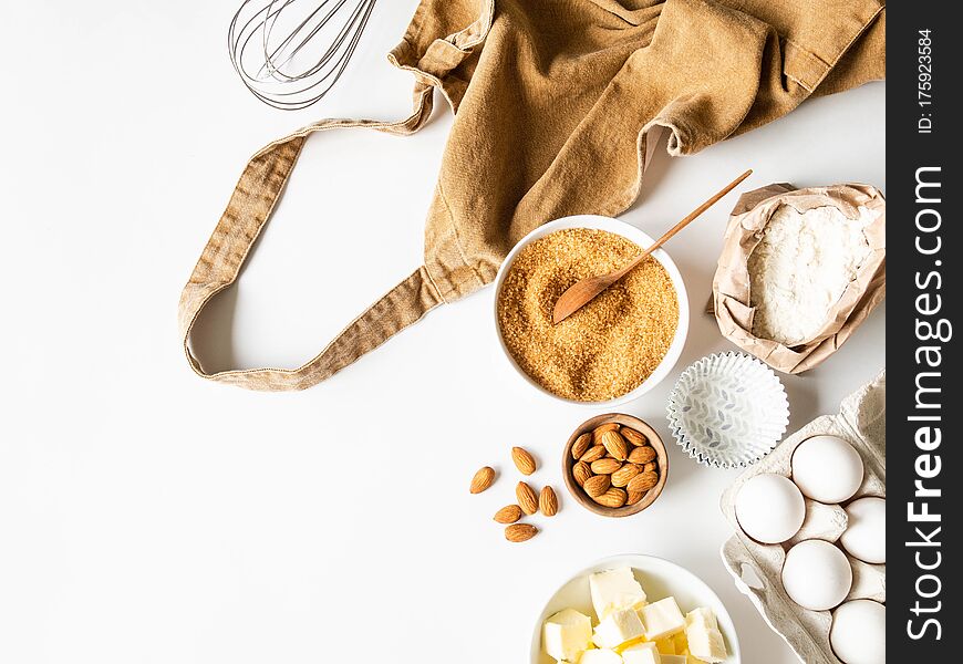 Ocher Apron And Various Baking Ingredients - Flour, Eggs, Sugar, Butter, Nuts On White Background. Top View