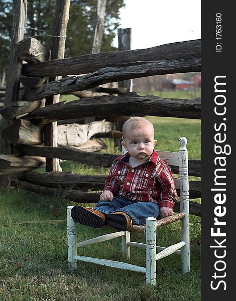 Image of baby boy sitting on a chair in front of a fence. Image of baby boy sitting on a chair in front of a fence