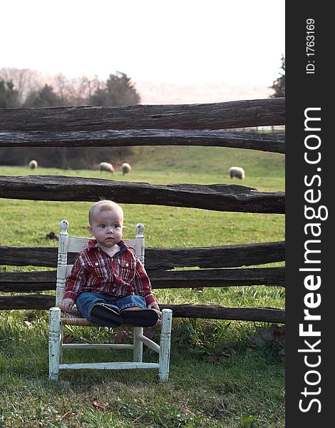 Image of baby boy sitting on a chair in front of a fence. Image of baby boy sitting on a chair in front of a fence