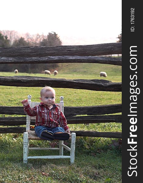 Image of baby boy sitting on a chair in front of a fence. Image of baby boy sitting on a chair in front of a fence