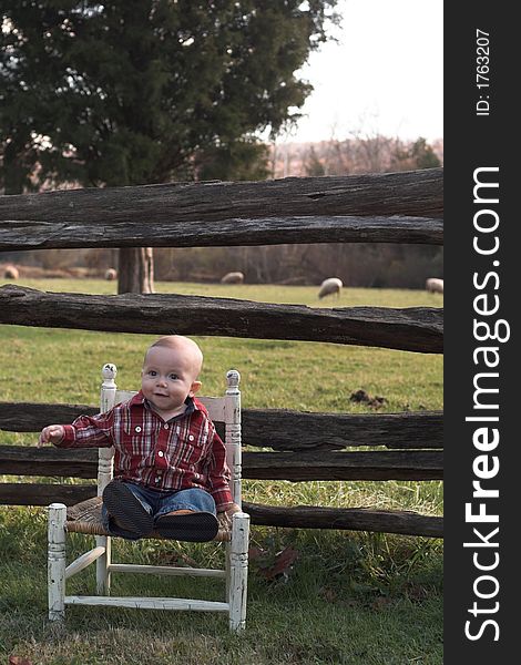 Image of baby boy sitting on a chair in front of a fence. Image of baby boy sitting on a chair in front of a fence