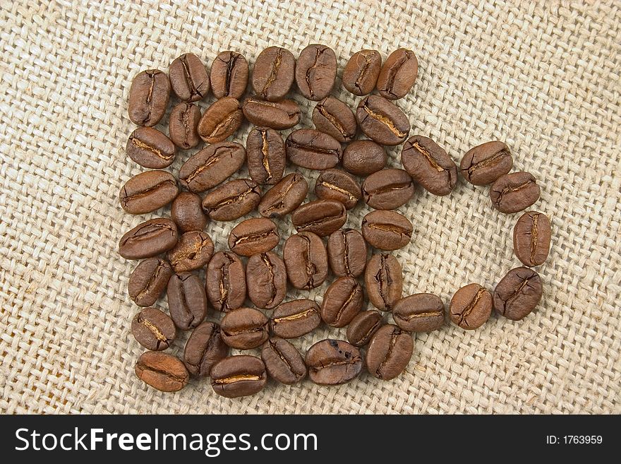 Mug made of coffee beans lying on flax background