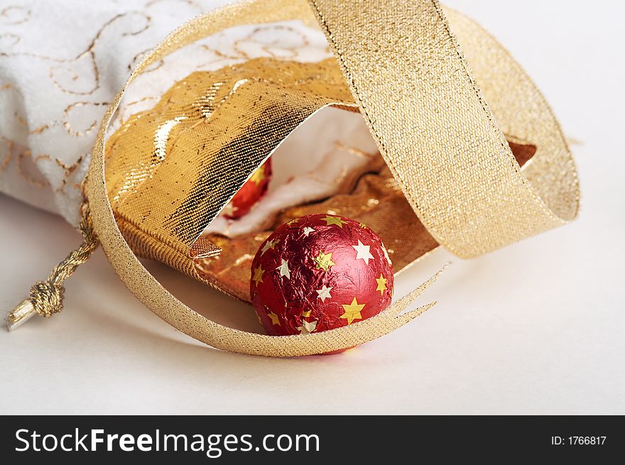 Chocolate candy in red metallic paper with stars lay near white & golden bag for gifts & golden strip on white background. Chocolate candy in red metallic paper with stars lay near white & golden bag for gifts & golden strip on white background.