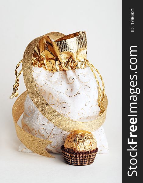 White and golden bag for gifts & golden sphere chocolate candy with golden strip stays at white background. White and golden bag for gifts & golden sphere chocolate candy with golden strip stays at white background.