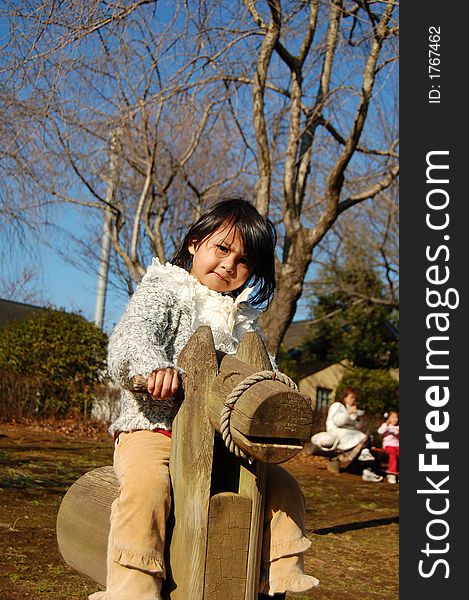A young asian girl rides wooden horse at park. A young asian girl rides wooden horse at park.