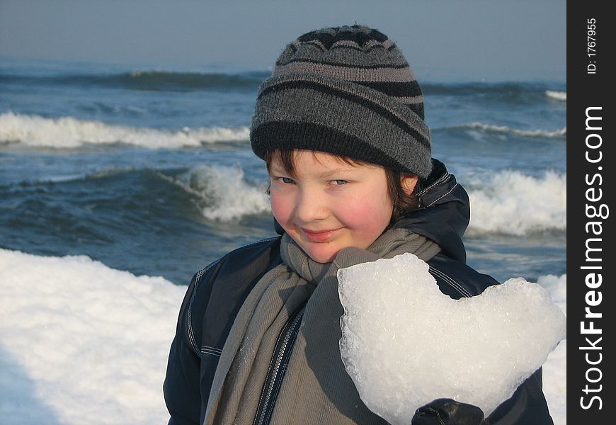 Smiling boy with ice heart in his hand is standing on the seashore.