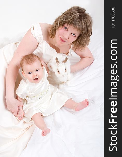 Mother and baby with rabbit are posing on white and looking into the camera
