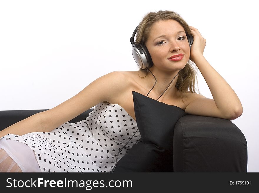 Young woman with headphones sitting on the black sofa. White background, in studio. Young woman with headphones sitting on the black sofa. White background, in studio.