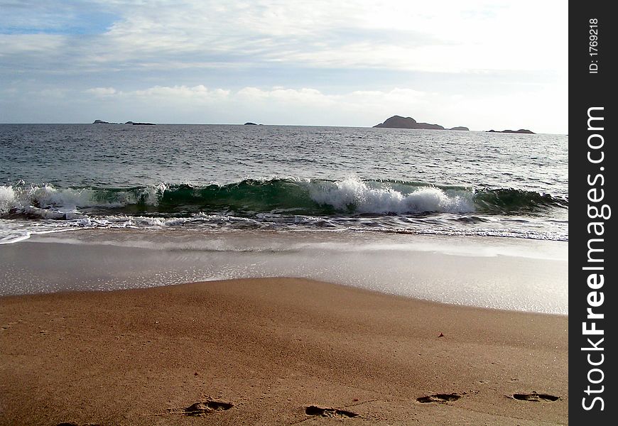 A wave crashes on shore on a beach. A wave crashes on shore on a beach