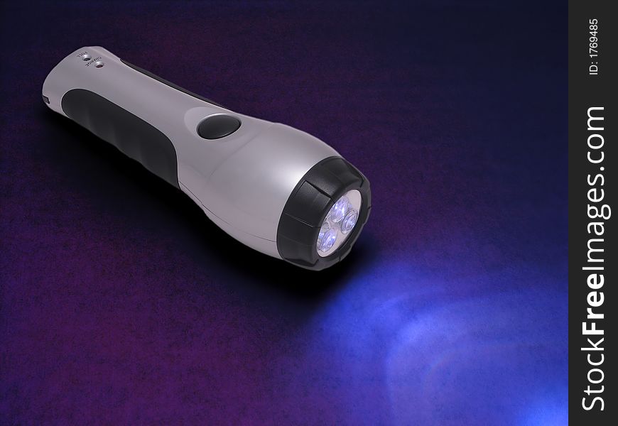 Glowing silver rechargeable flashlight on blue surface. Glowing silver rechargeable flashlight on blue surface