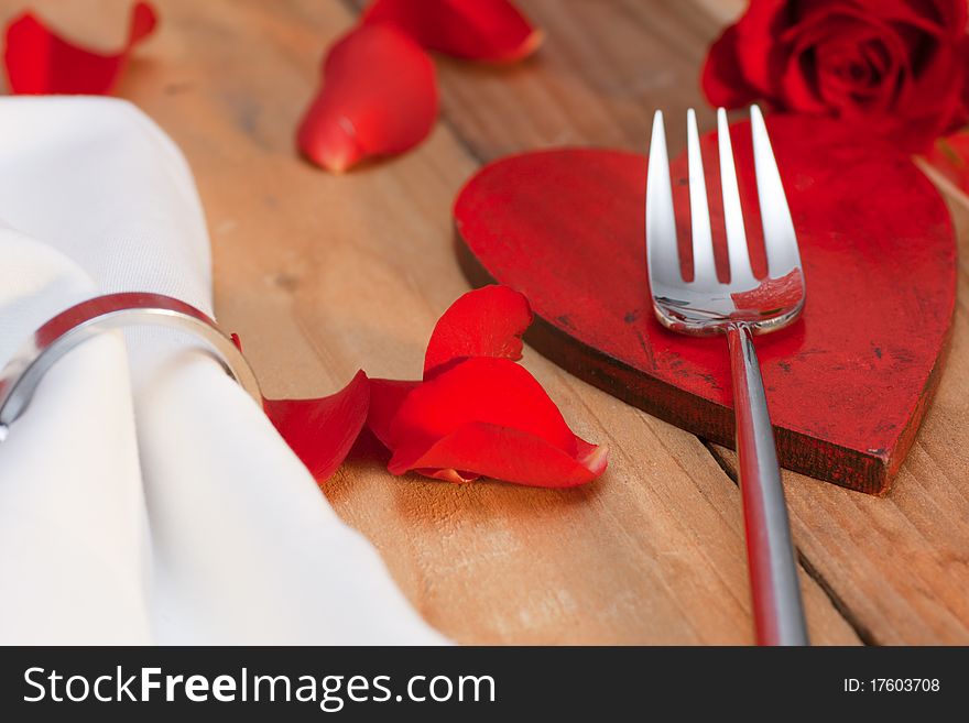 Place setting with red petals on a wooden table in country style. Place setting with red petals on a wooden table in country style