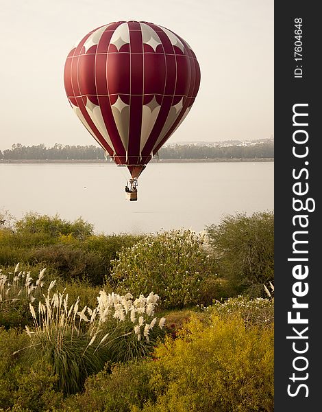 Red, white, and silver balloon over lake with plant vegetation in foreground. Red, white, and silver balloon over lake with plant vegetation in foreground