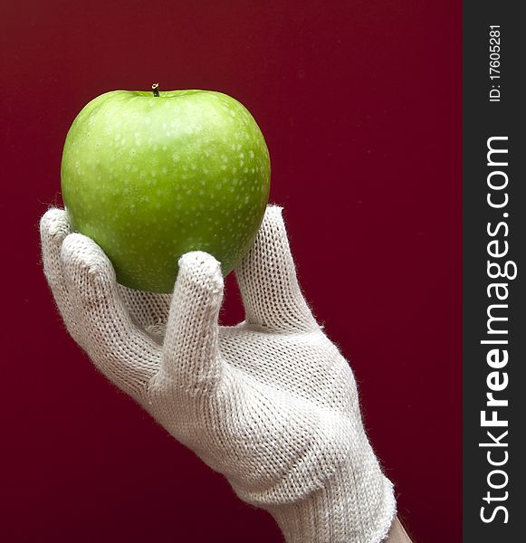 A hand in white glove holding an apple on red background