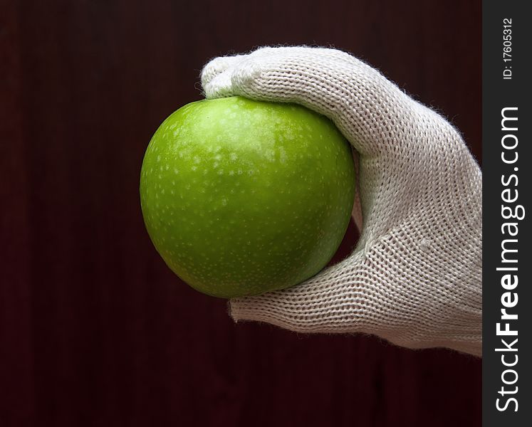 A hand in white glove holding an apple on dark background