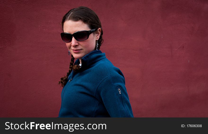 Young woman in sun glasses with braids in blue sweater on red background. Young woman in sun glasses with braids in blue sweater on red background