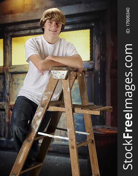 A happy teen boy hangomg on a ladder in a grungy old garage. A happy teen boy hangomg on a ladder in a grungy old garage.