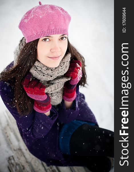 Attractive brunette young woman sitting on a bench on snowy day. Attractive brunette young woman sitting on a bench on snowy day