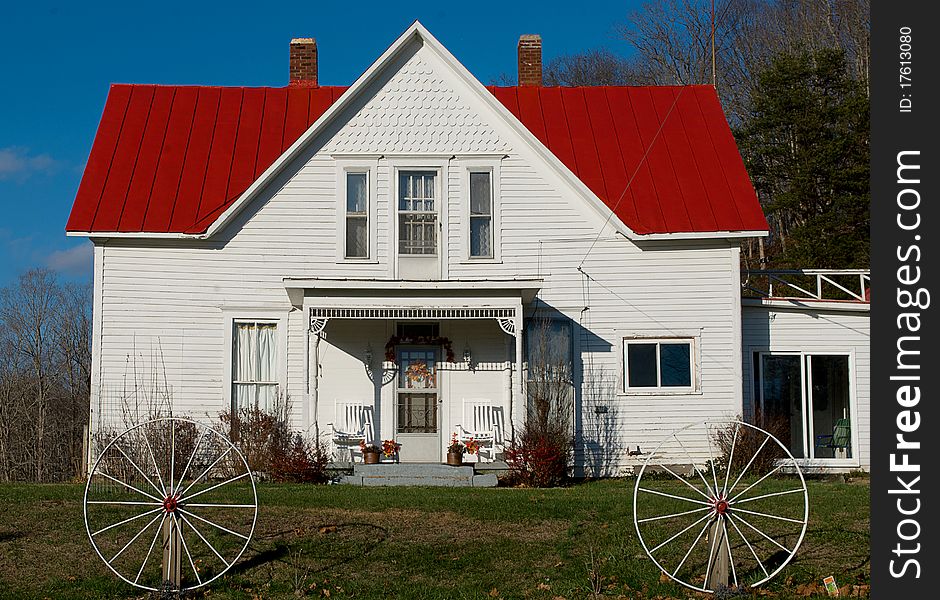 Rural wooden white house with a red roof and two horse-cart wheels. Rural wooden white house with a red roof and two horse-cart wheels