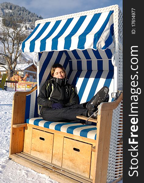 Young woman sleeping in roofed wicker beach chair on a sunny winter day in austria.