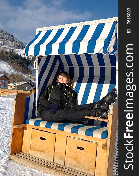 Young woman sleeping in roofed wicker beach chair on a sunny winter day in austria.