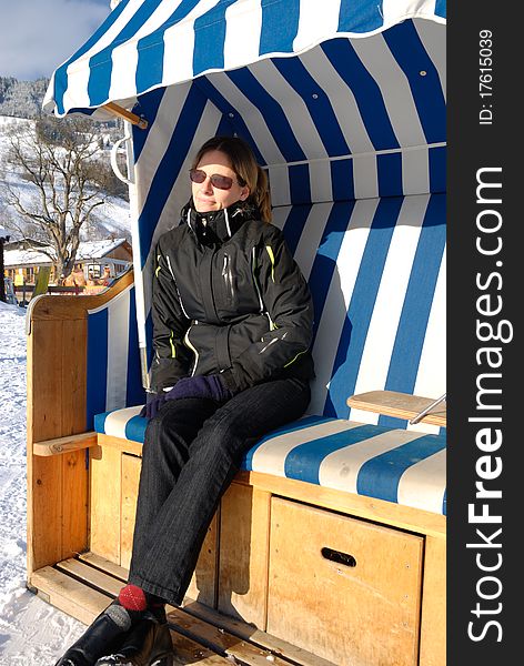 Young woman relaxing in roofed wicker beach chair on a sunny winter day in austria.