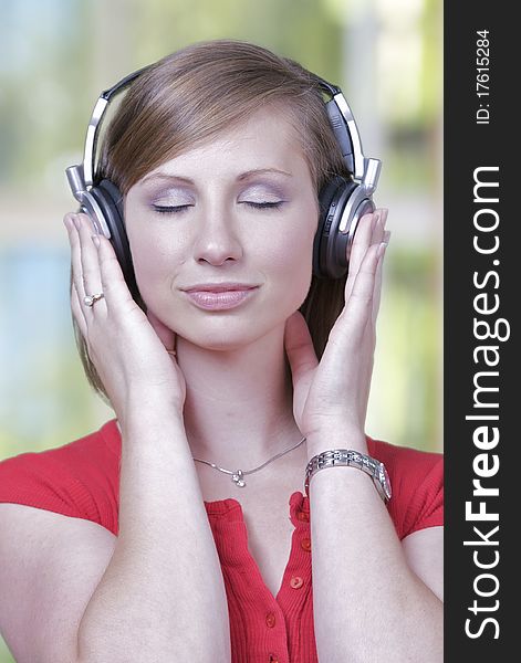 A caucasian woman listens to music on a headset, set against a green window background.