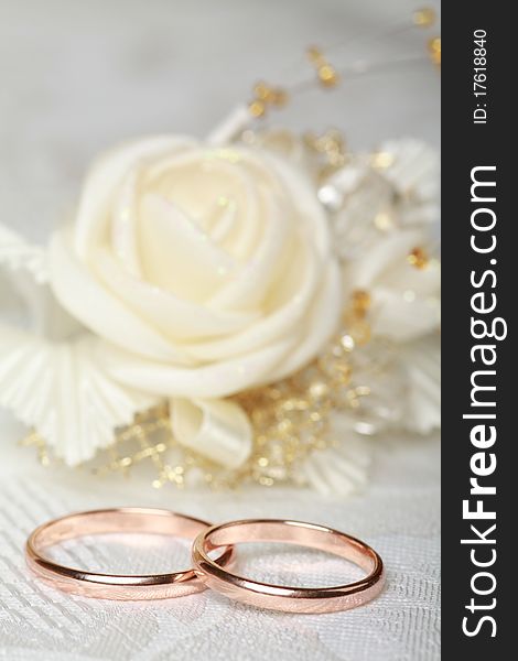 Gold wedding rings and satin rose flower on lace background