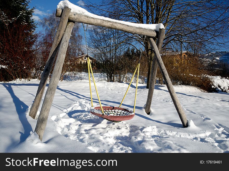 Snow covered swing at empty playground in winter.
