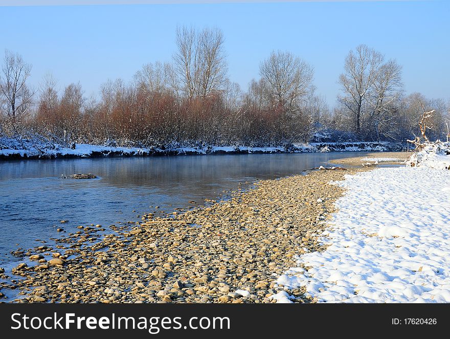 Curved rocky river covered by snow in a sunny winter day