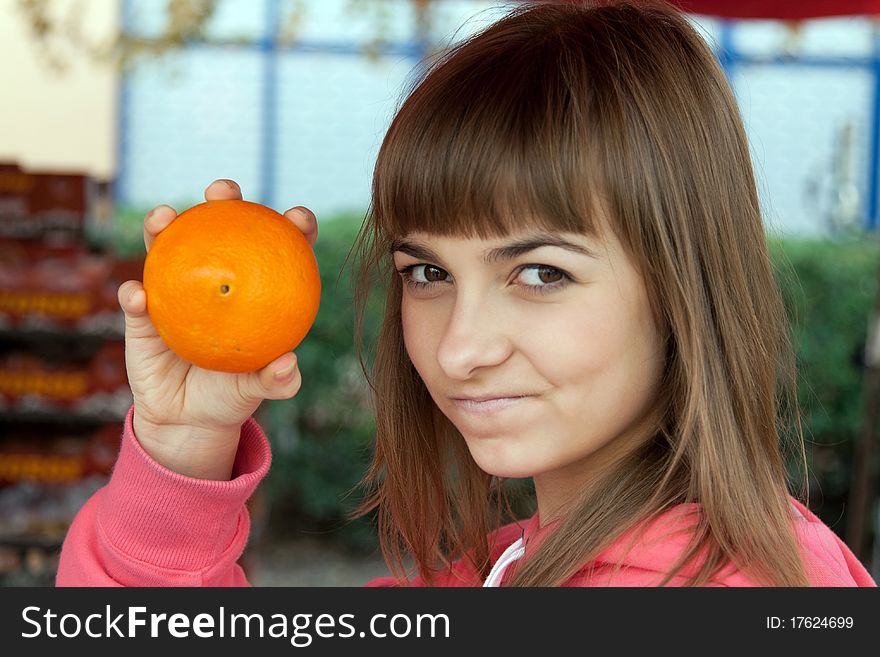Beautiful girl with an orange at the bazaar