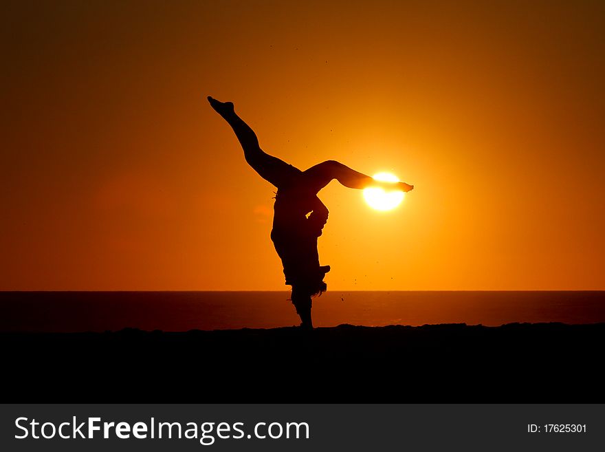 Silhouette of gymnast on beach at sunset