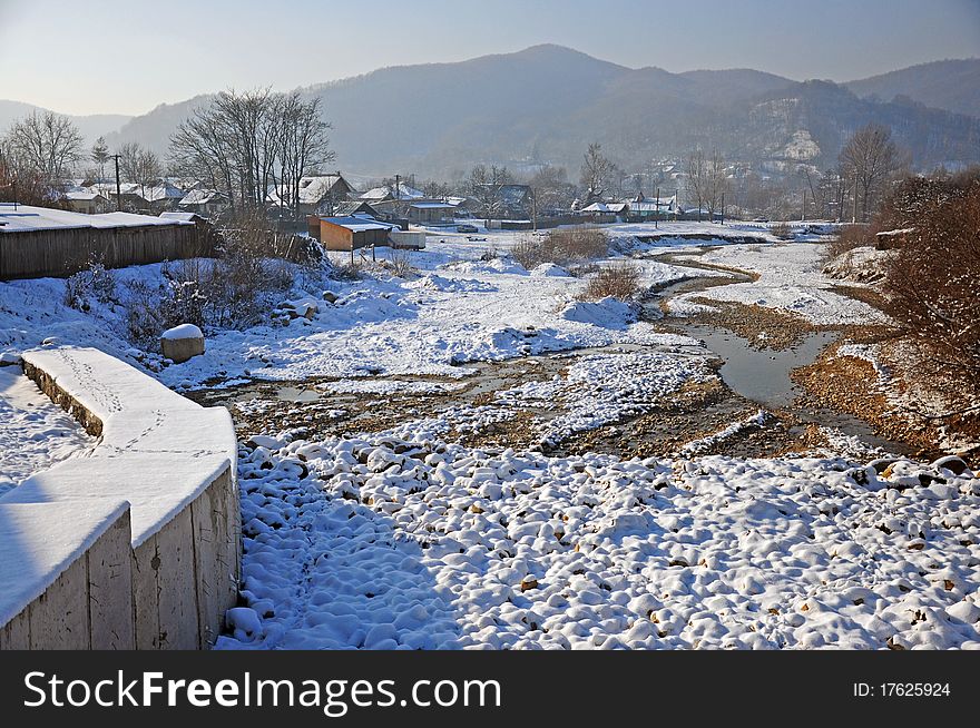 Village on snowy river valley in sunny winter day