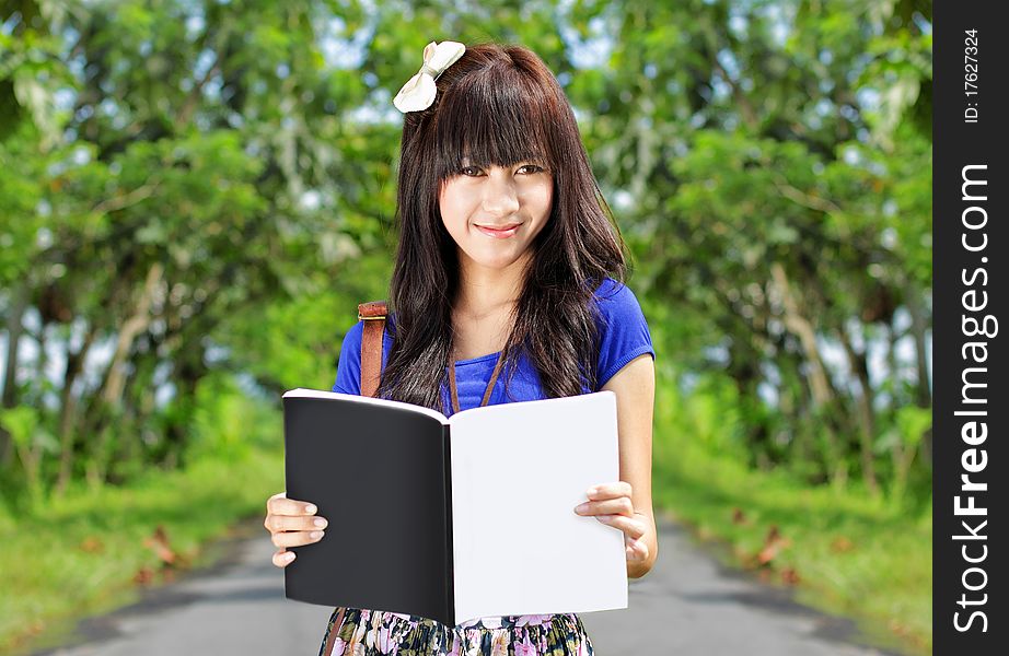 Happy young girl smiling while holding and reading a book. Happy young girl smiling while holding and reading a book
