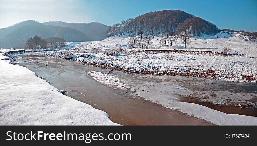 Curved river on snowy valley near forest in sunny winter day