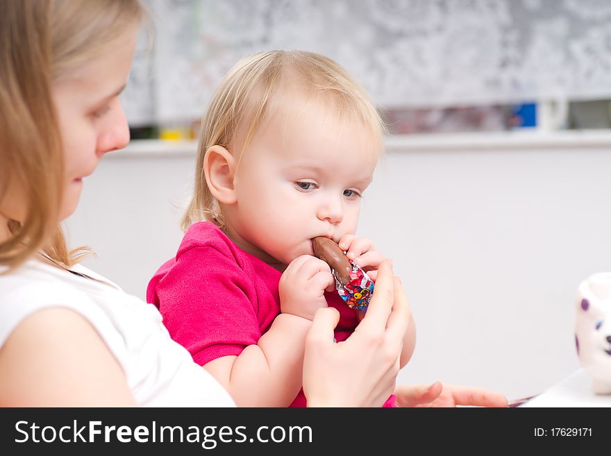 Young adorable baby eat chocolate with mother in kitchen