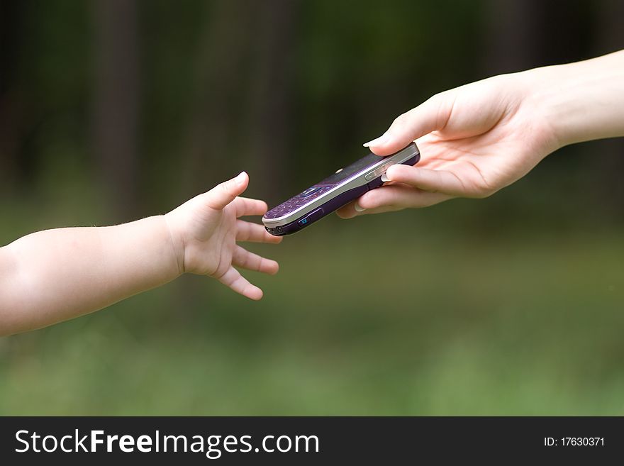 Female hand Giving cellphone to the child`s hand on the forest background