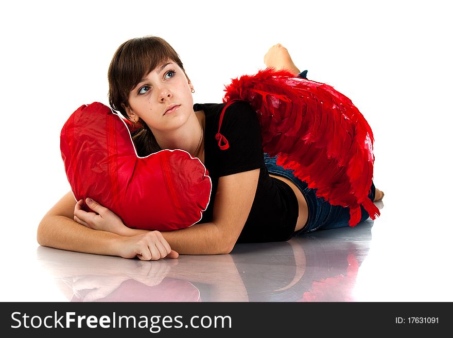 Beautiful girl lying with heart shaped red pillow in red angel wings isolated on white. Beautiful girl lying with heart shaped red pillow in red angel wings isolated on white