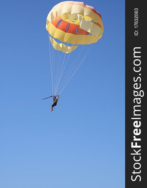A parasailer attached to a parachute and a tow line against blue sky. A parasailer attached to a parachute and a tow line against blue sky.