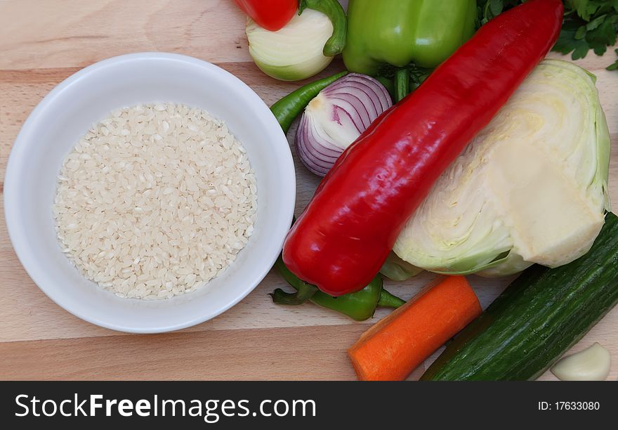 Upper view of a bowl of rice near fresh vegetables on a choping board. Upper view of a bowl of rice near fresh vegetables on a choping board.