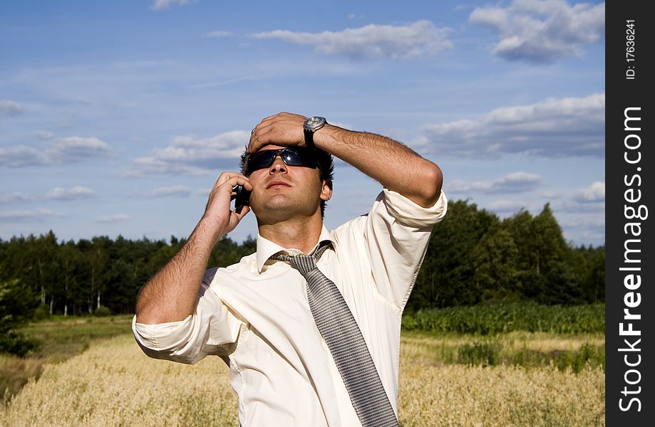 A businessman dressed in a smart suit standing on grass and talking on mobile phone.