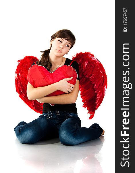 Beautiful girl sitting with heart shaped red pillow in red angel wings isolated on white