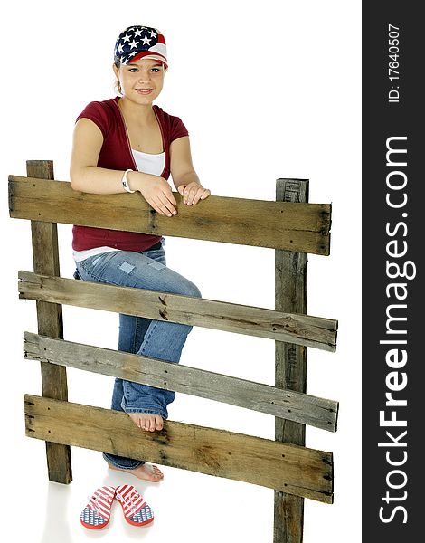 A happy young teen in a stars and stripes hat leaning on an old rail fence. Isolated on white. A happy young teen in a stars and stripes hat leaning on an old rail fence. Isolated on white.