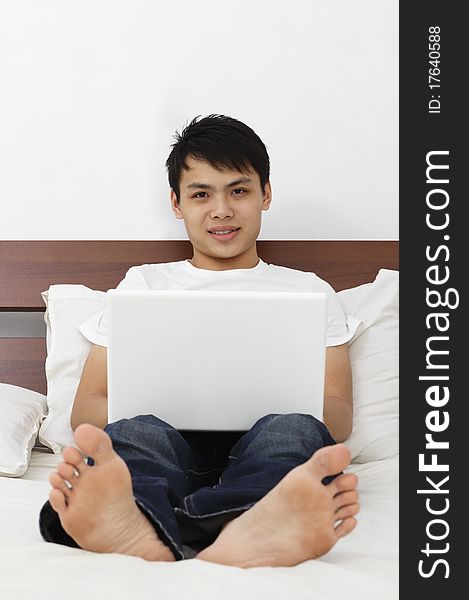 Young Asian man with laptop on a bed
