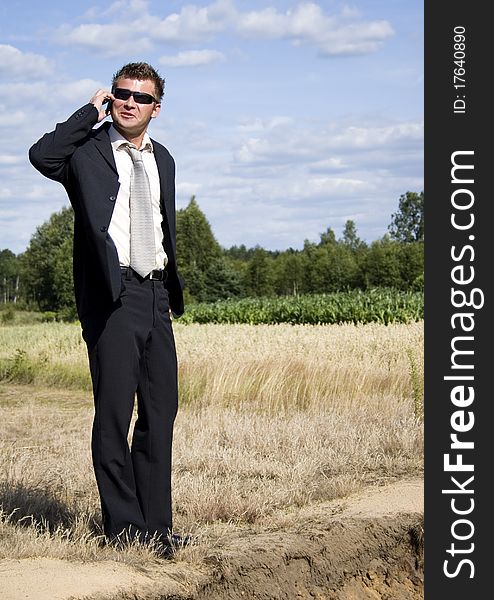 A businessman dressed in a smart suit standing on grass. Businessman talking on mobile phone
