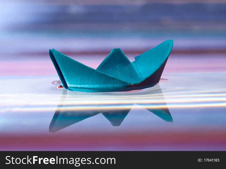 Blue paper boat and reflection on water, beautiful purple background