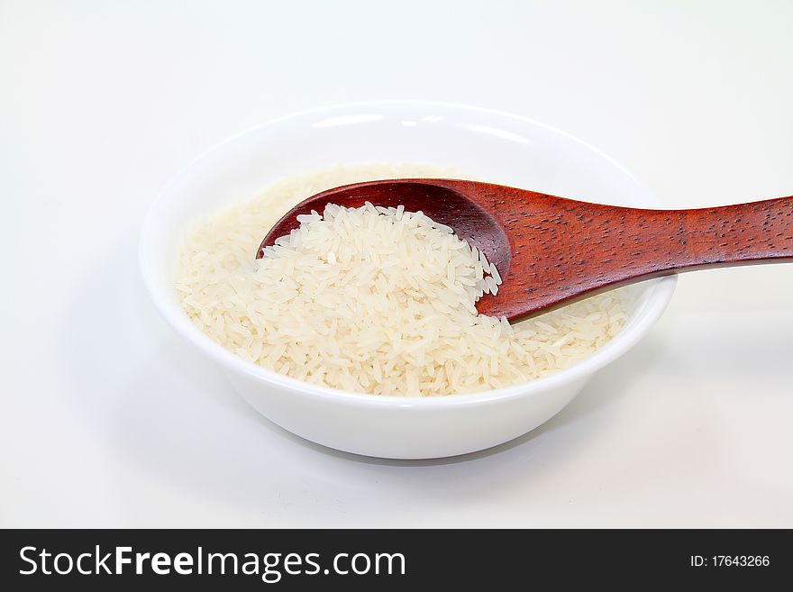 Rice grains in white bowl with brown wood spoon; white background.